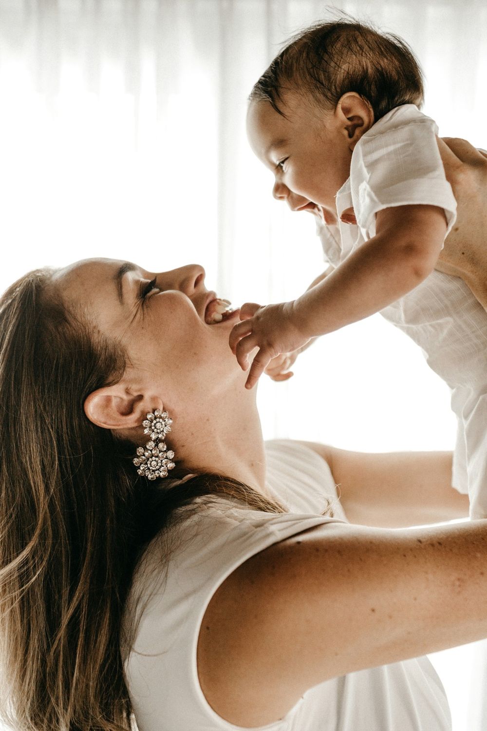 A mother laughing as she lifts her baby up towards her