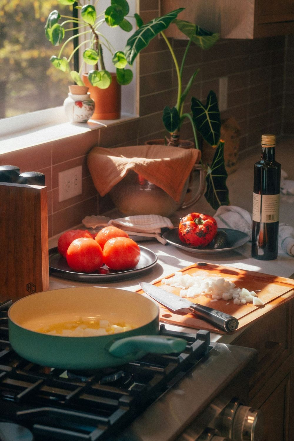 A sunny kitchen with tomatoes, a roasted pepper and chopped onion ready for cooking